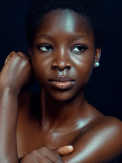 A young Black woman with luminous skin against a deep navy background
