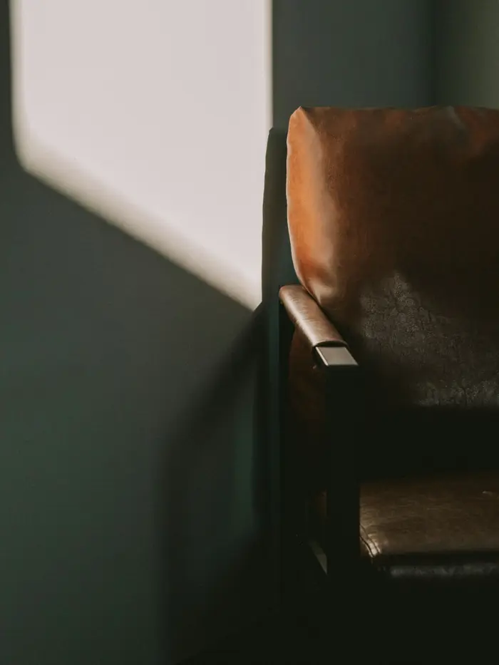 A leather armchair in the corner of a dark green room, a patch of light on the wall