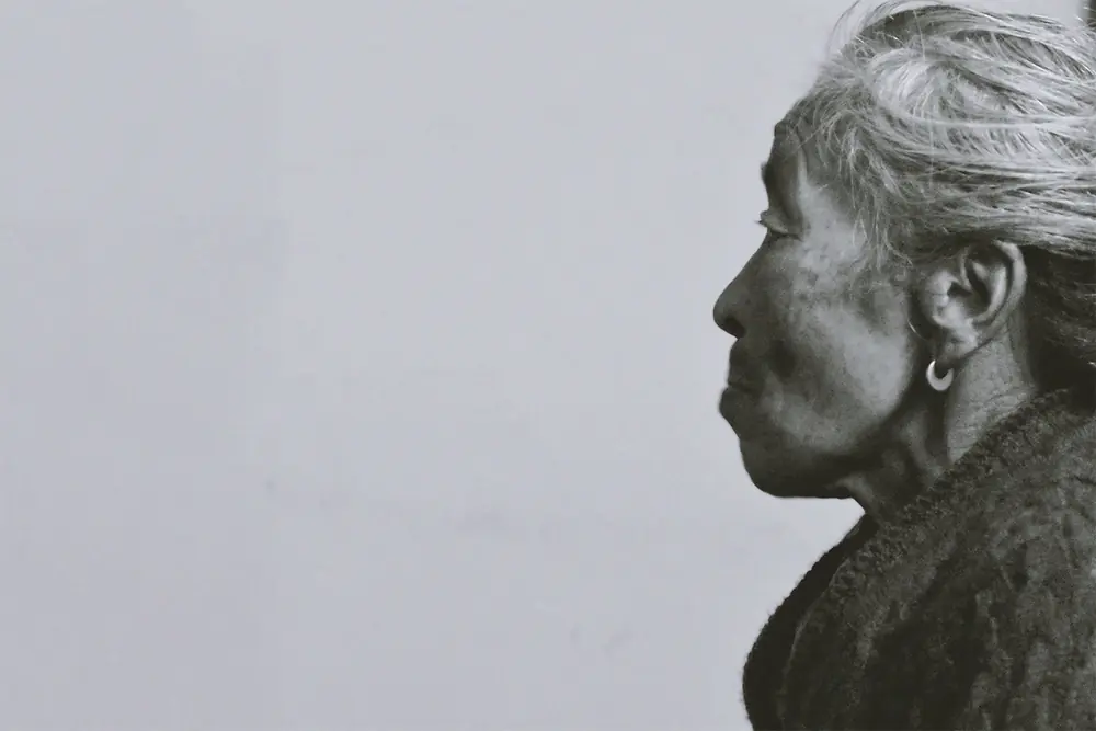 Black-and-white profile of an older woman with silver hair against a pale wall