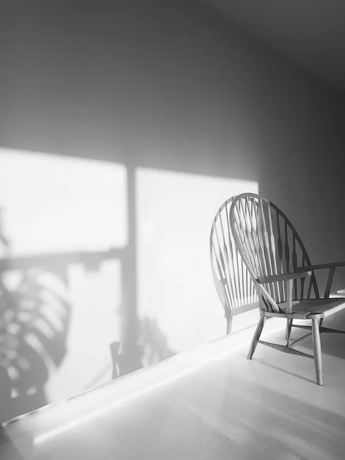 A single wooden armchair in a quiet room, afternoon light falling across the wall